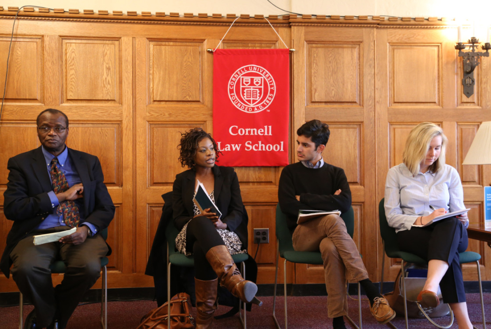 four people, presenting, seated in front of a Cornell Law school flag